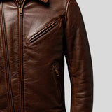 A close-up of a brown leather jacket showing the front zipper, chest zip pocket, and side zip pocket against a light gray background.