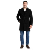 A man modeling a black mid-length coat over a white shirt, blue jeans, and brown shoes, photographed against a plain white background.