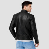 A man wearing a black leather jacket, shown from the back, paired with light blue jeans against a solid light gray background.