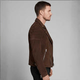 A man in profile wearing a dark brown suede biker jacket with silver zippers, paired with black pants, against a solid gray studio background.