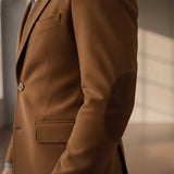 Close-up of a person wearing a camel brown blazer with dark brown elbow patches, showing the fabric texture and button detail.