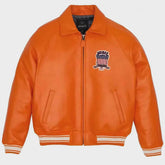 An orange leather jacket with a zip-up front, ribbed collar, cuffs, and hem, featuring a patriotic American flag patch on the left chest. The brand name 'AVIREEZ' is visible on the inner neck label and the patch.