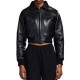 A model wearing a black faux-leather cropped zip-up jacket with a tonal black embroidered logo on the left chest, paired with black sweatpants, against a plain white background.