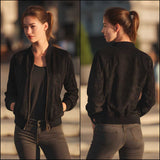 A woman modeling a black bomber jacket in a split front and back view, shown outdoors in warm golden-hour light.