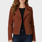 A woman wearing a brown suede-bike-style jacket over a black top and dark blue jeans, shown from the lips down against a light gray studio background.