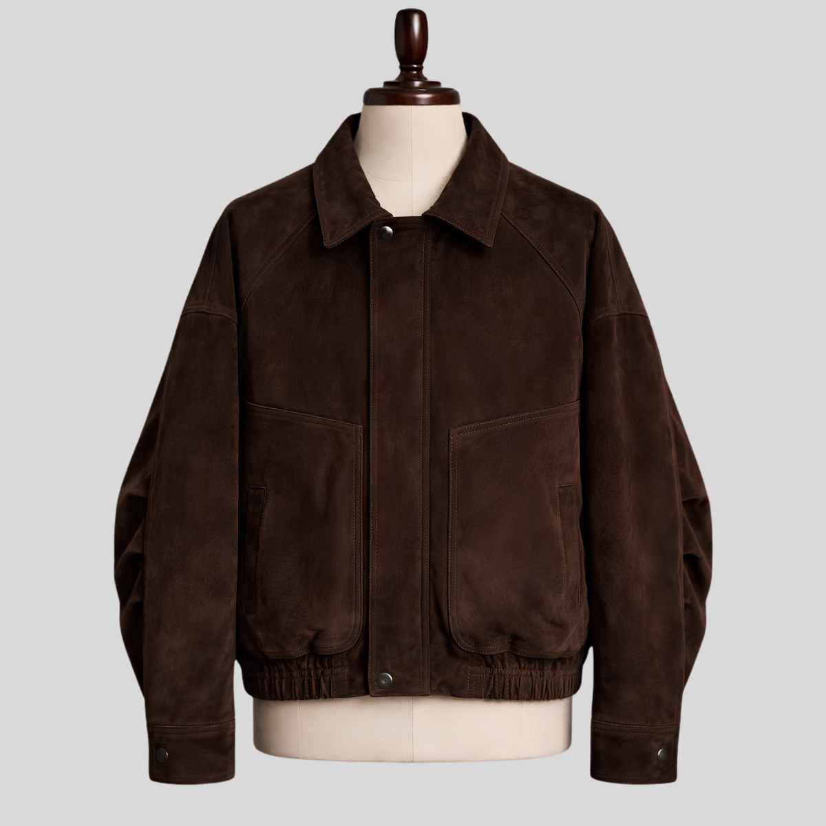 A dark brown suede utility jacket displayed on a cream-colored mannequin torso with a wooden neck cap, set against a solid light gray background.