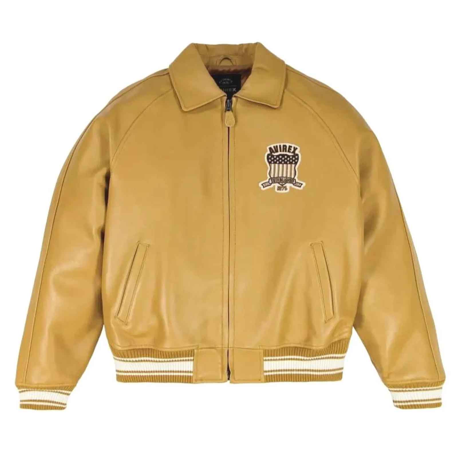 A tan leather varsity-style jacket with a front zipper, ribbed knit collar, cuffs, and hem, featuring a black, white, and red embroidered 'ANJIRE' graphic on the left chest, displayed on a clean white background.