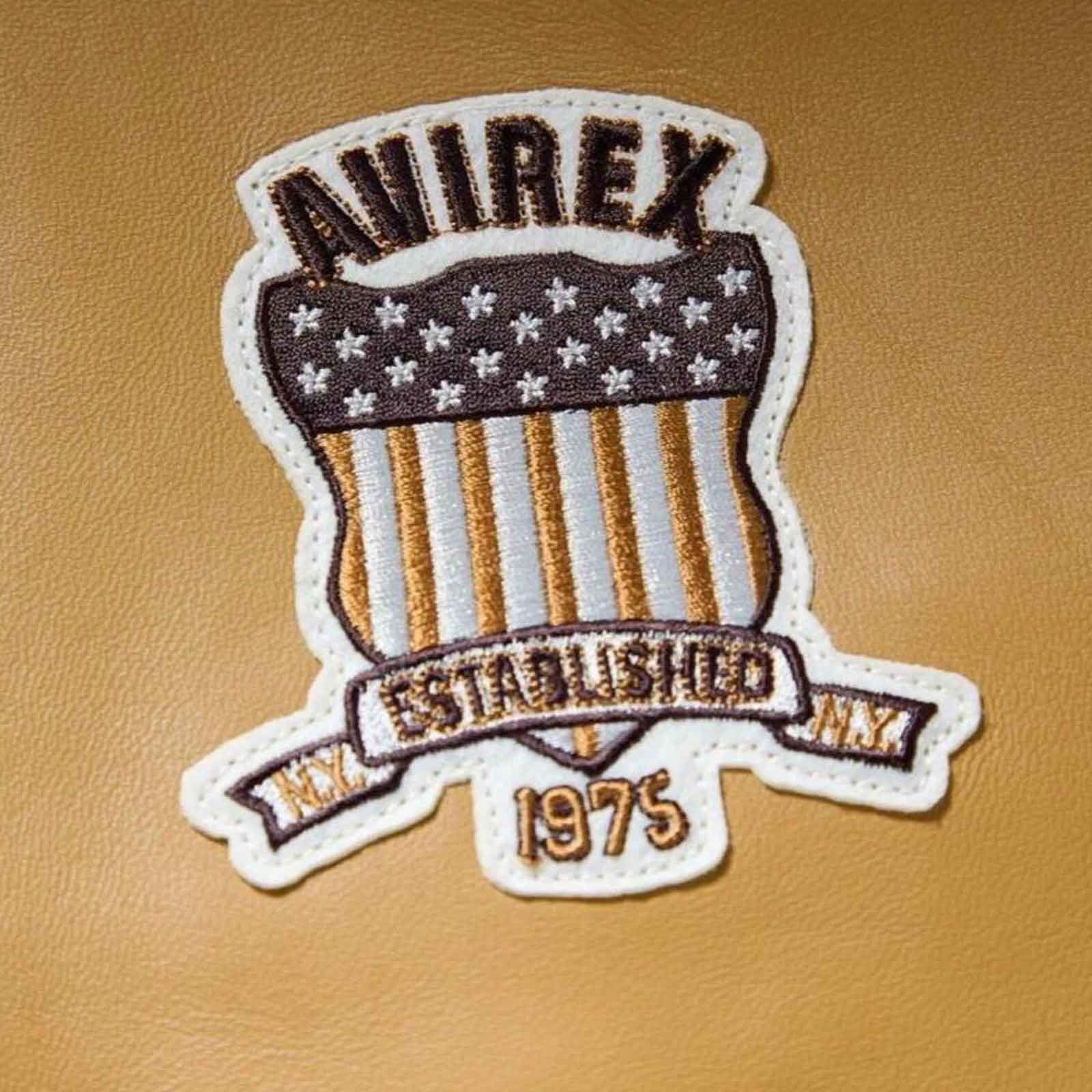 An embroidered shield-shaped patch with the word 'AWIREX' at the top, a dark brown top section with white stars, vertical tan and white stripes, a banner reading 'EST. 1975', and 'N.