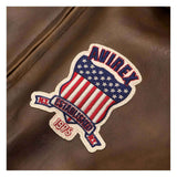 A close-up of a brown leather jacket featuring a decorative embroidered patch with the brand name 'AUREX', an American flag motif, and 'EST. 1975'.
