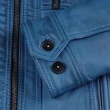 Close-up detail of a blue leather jacket showing a flap pocket with two black snap buttons and a black zipper.