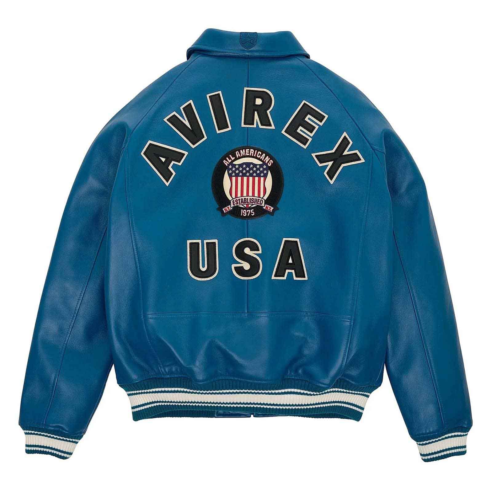 A blue leather jacket shown from the back, featuring 'AVIREX USA' and an 'All Americans 1915-1945' crest patch in large varsity-style lettering. The jacket has white and navy striped ribbed cuffs and hem.
