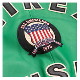 A close-up of a green leather patch featuring a circular 'All Americans Established 1975' emblem with an American flag design, surrounded by partial black and white lettering.