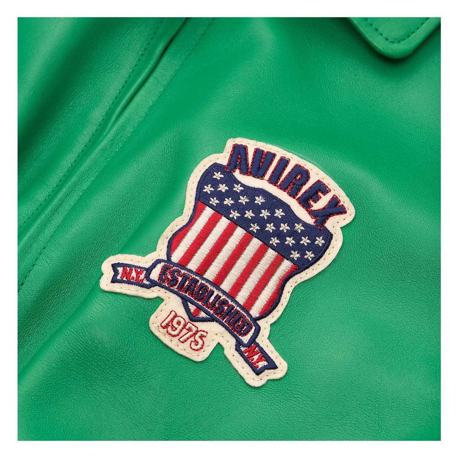 A close-up of a green leather jacket featuring a decorative embroidered patch with an American flag design, the word 'AVIREX,' and 'EST. 1975.