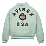 A mint green leather jacket shown from the back, featuring 'AVIREX USA' and a circular 'All Americans 1975' patch on the back. The jacket has ribbed cuffs and hem with white and dark green stripes.
