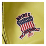 A close-up of a yellow-green faux leather surface featuring a decorative embroidered patch with the brand name 'ANIREX' and a shield design in red, white, and blue with the text 'ESTABLISHED NY 1975' and a zipper running along the left edge.