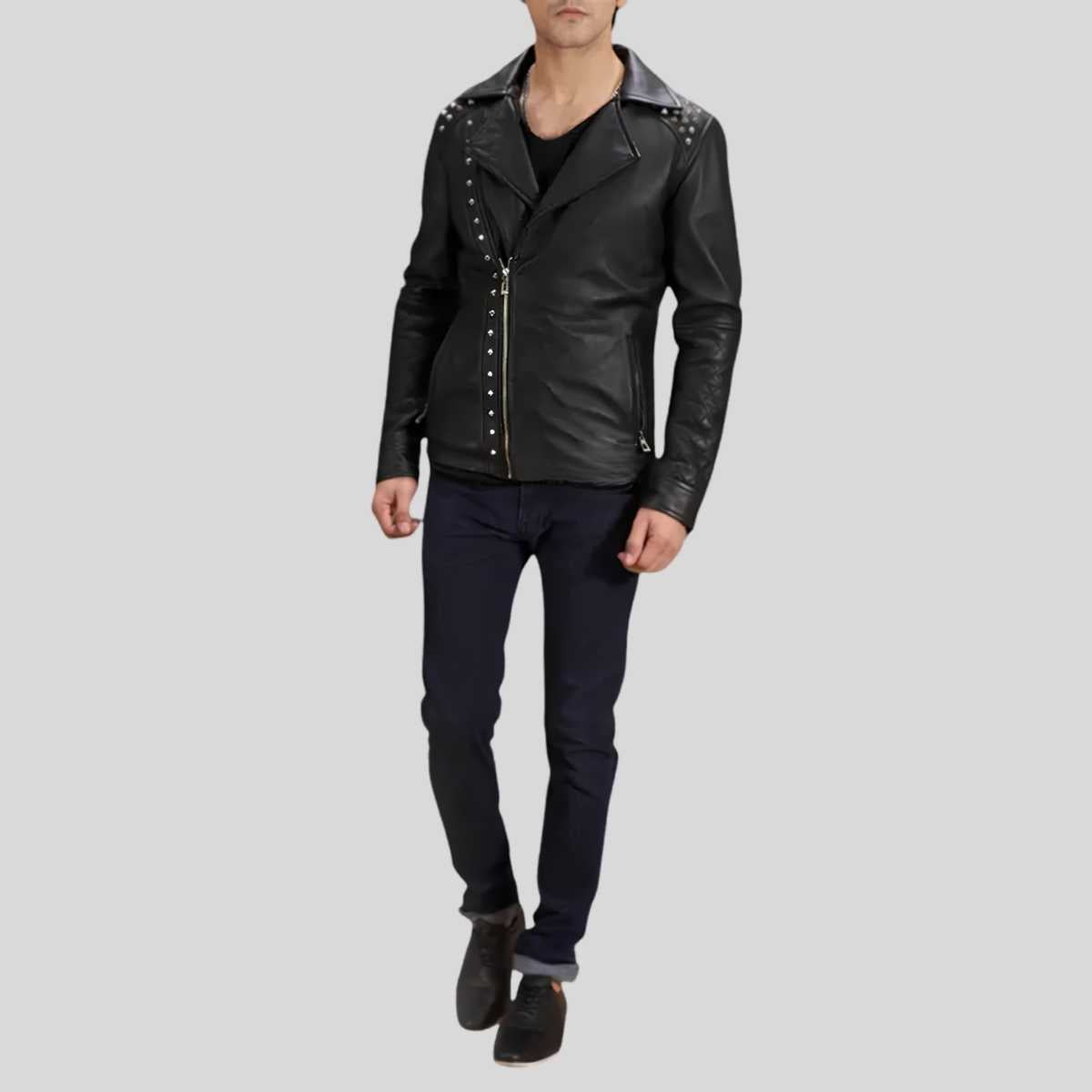 A man wearing a black leather motorcycle jacket with silver studs and a front zipper, paired with dark jeans and black shoes, shown against a solid gray background.
