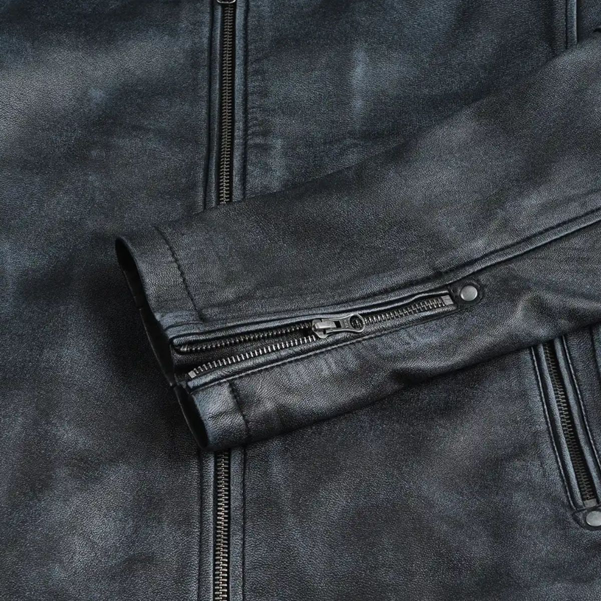 Close-up of a dark gray leather jacket showing the sleeve cuff with a zippered pocket and a vertical front zipper.