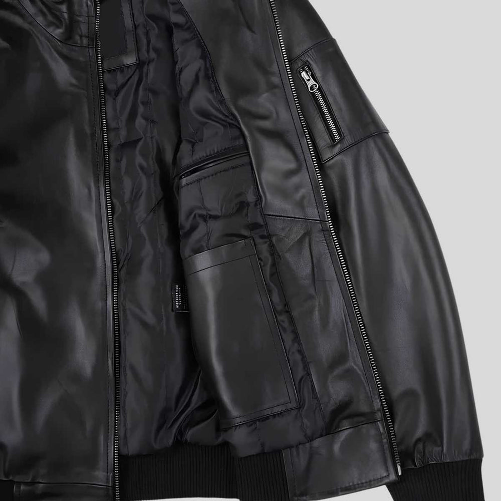 Close-up of a black leather bomber jacket showing the front zipper, interior lining, zippered pocket, and ribbed hem and cuffs on a light gray background.
