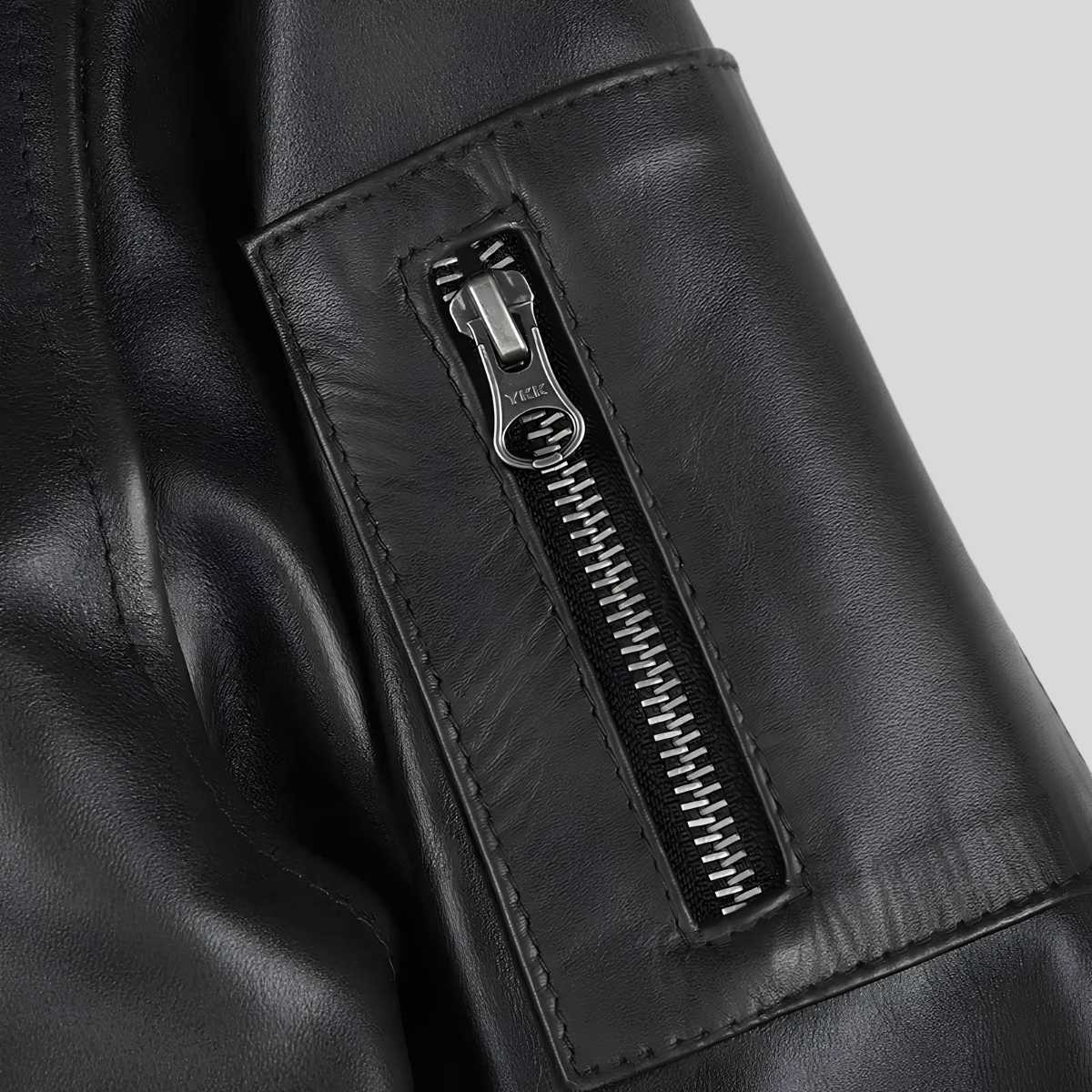 Close-up of a black leather jacket featuring a vertical zippered pocket with a silver-toned metal zipper pull.