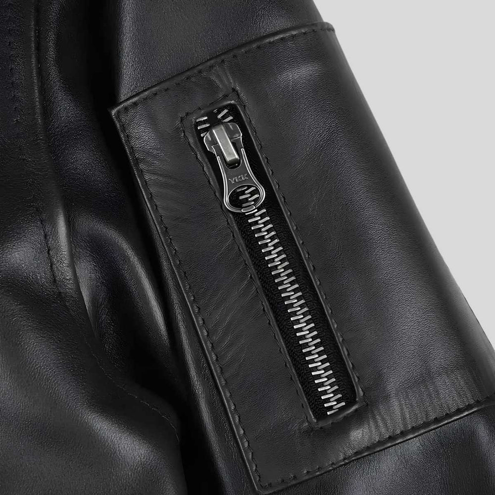 Close-up of a black leather jacket featuring a vertical zippered pocket with a silver-toned metal zipper pull.
