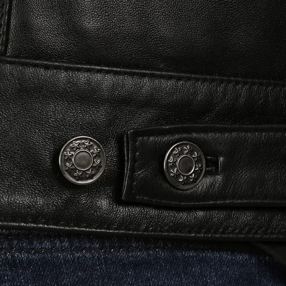 Close-up of a black leather jacket detail showing two round silver-tone decorative buttons on a strap, with dark blue denim visible below.