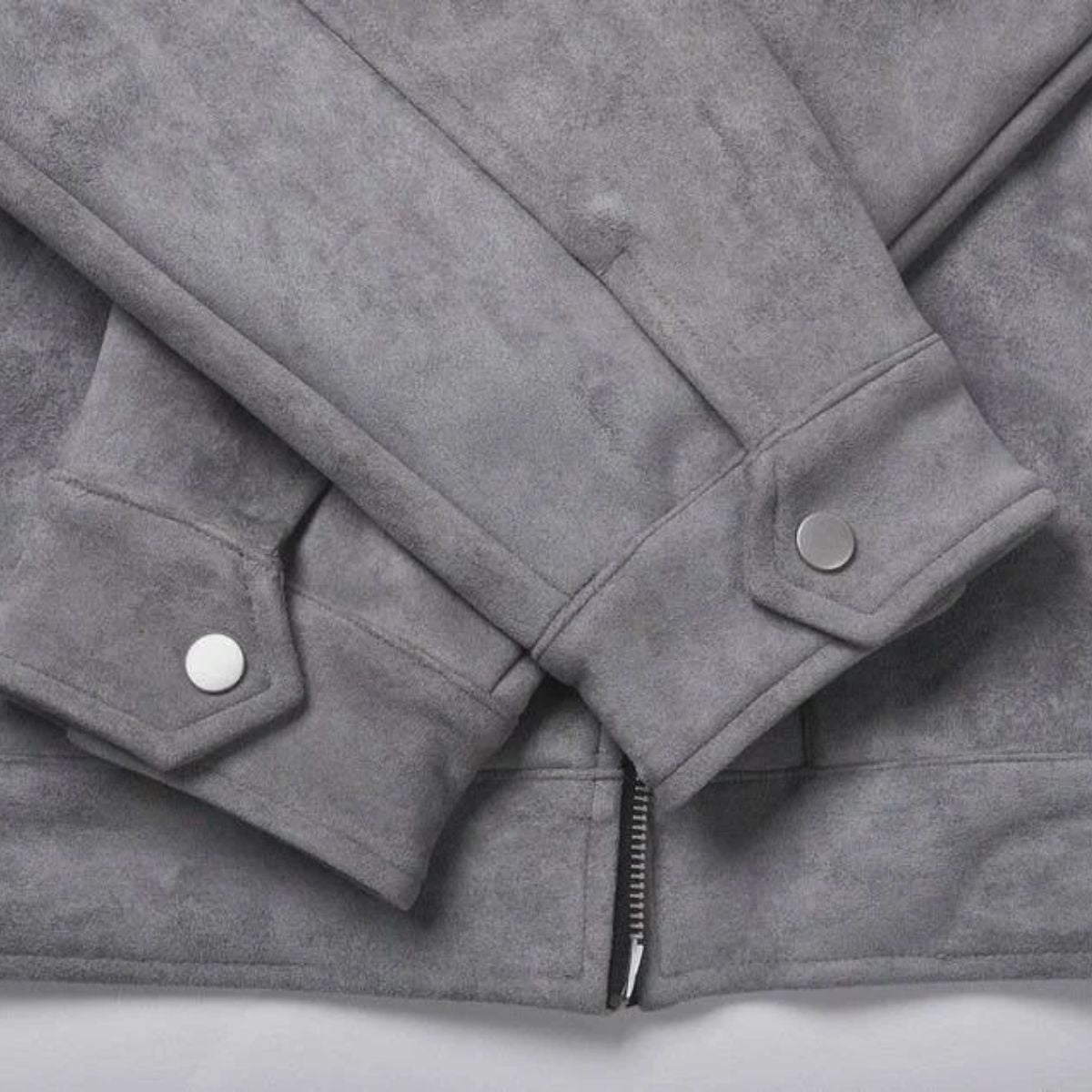Close-up of a gray suede jacket showing the sleeve cuffs with silver snap buttons and a zipper detail at the bottom.