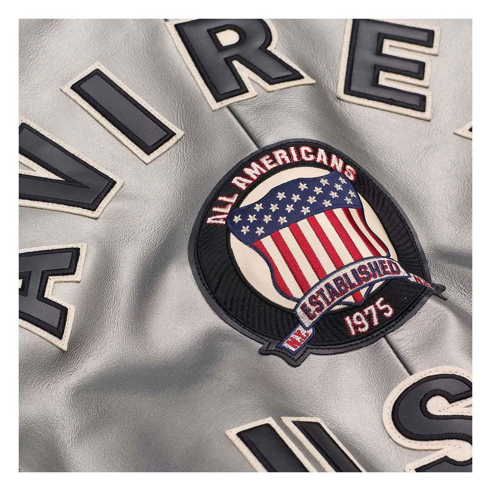 Close-up of a silver leather jacket featuring a circular 'All Americans' patch with an American flag design and 'Established 1975' text, surrounded by large black and white lettering.