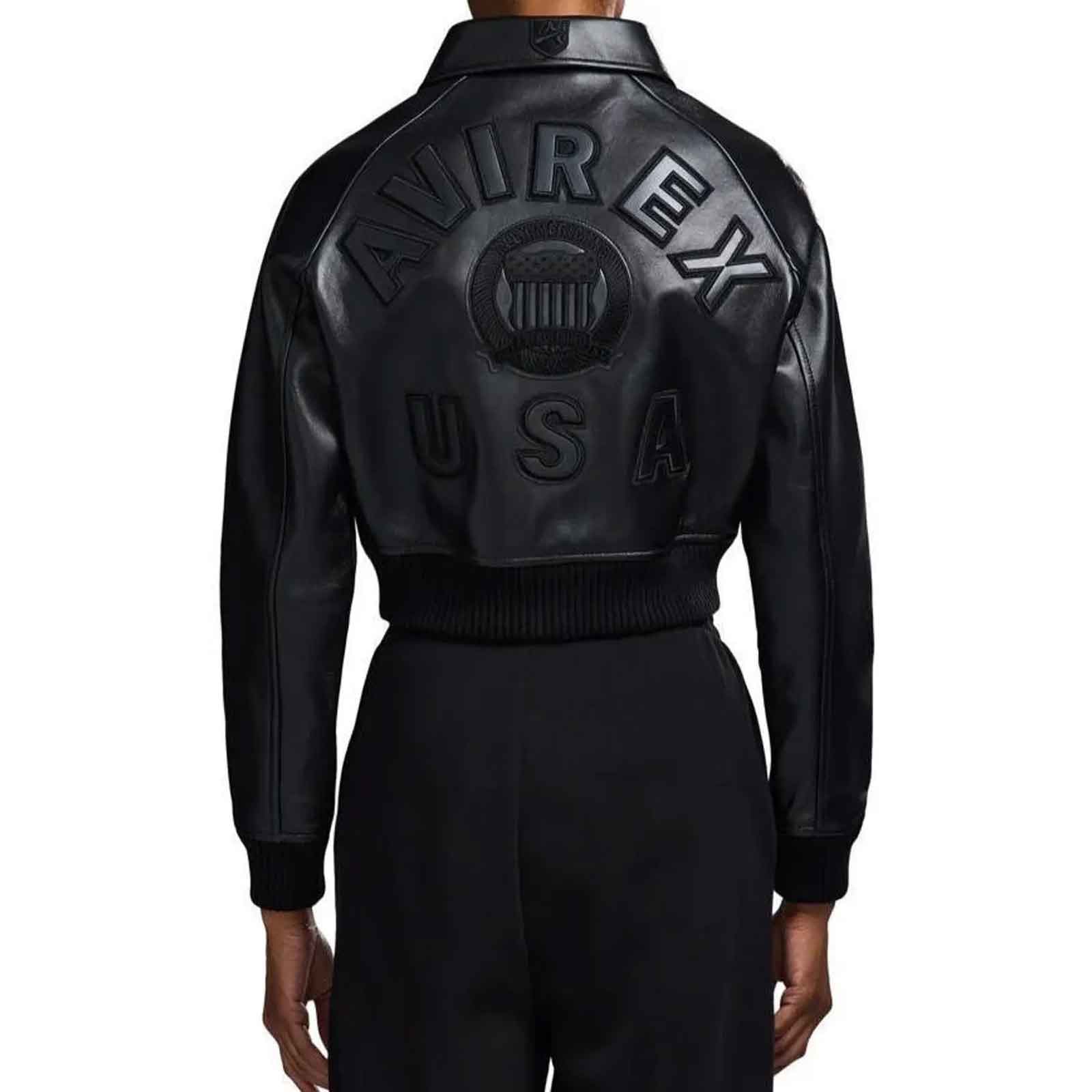 Back view of a person wearing a black leather bomber jacket with large embossed 'AVIREX USA' lettering across the back, paired with black pants, on a plain white background.