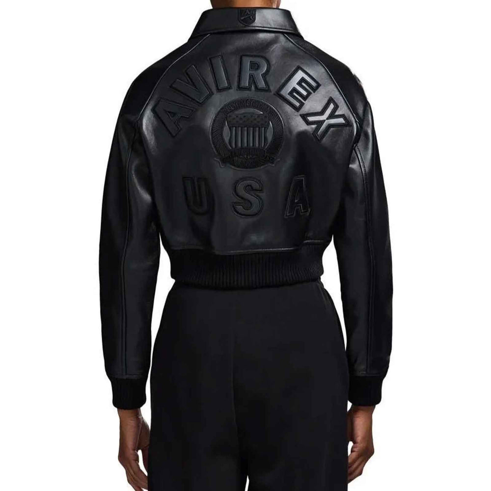 Back view of a person wearing a black leather bomber jacket with large embossed 'AVIREX USA' lettering across the back, paired with black pants, on a plain white background.