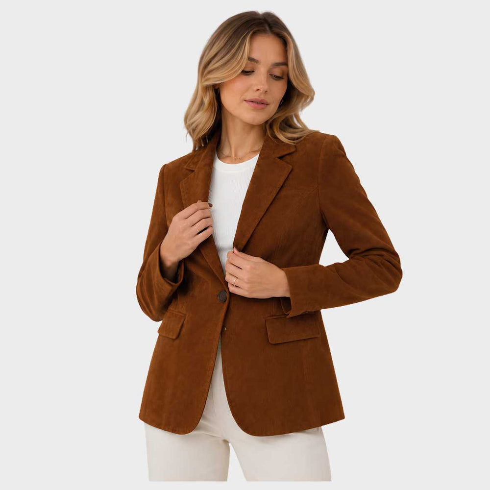 A woman wearing a brown suede blazer over a white top and white pants, standing against a light gray studio background.