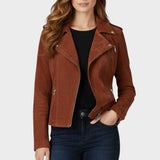 A woman wearing a brown suede moto jacket over a black top and dark blue jeans, shown from the lips down against a light gray background.