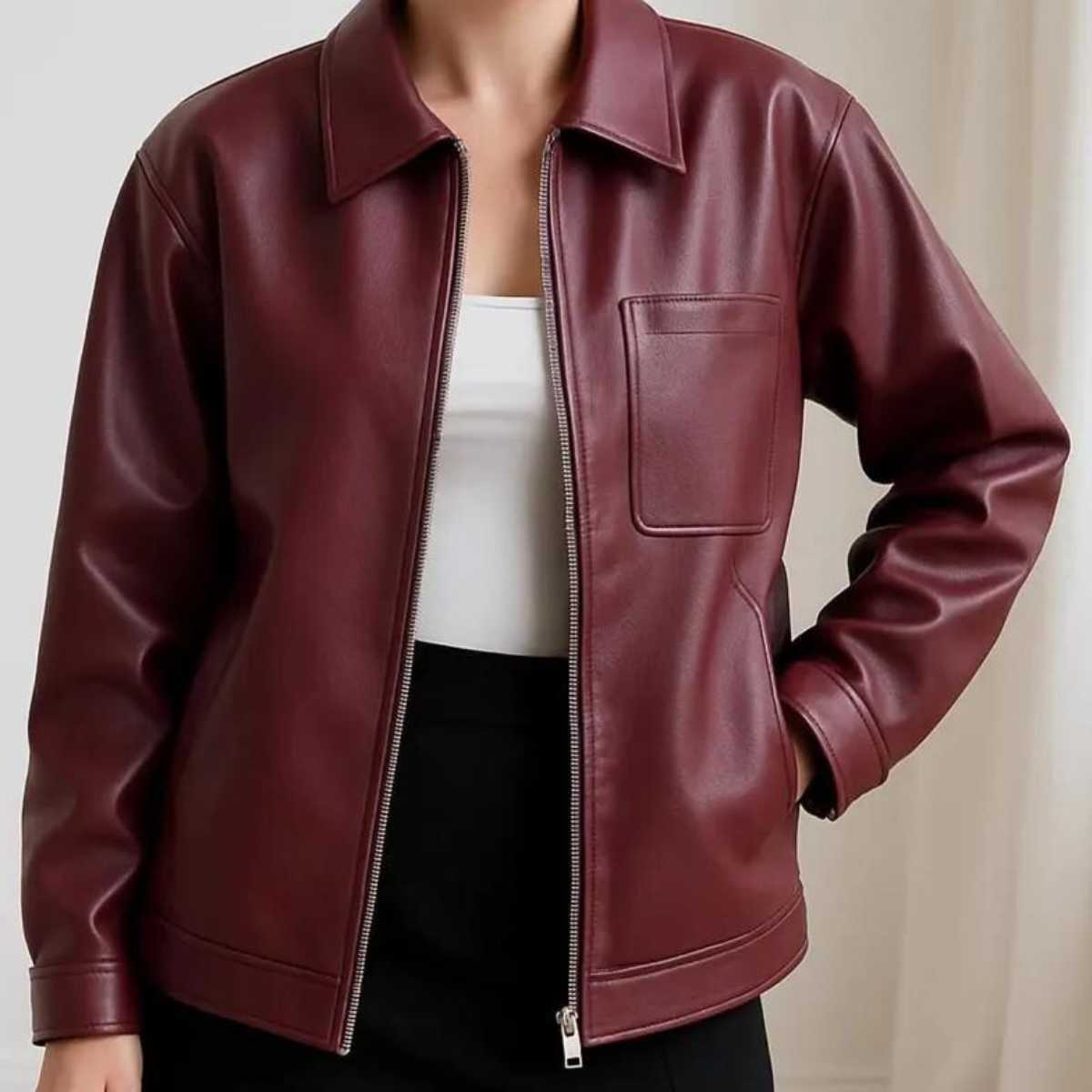 A person wearing a burgundy faux leather jacket over a white top and black bottoms, shown from the neck down against a light neutral indoor background.