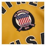 Close-up of a yellow garment featuring a circular embroidered patch with an American flag design and the text 'ALL AMERICANS ESTABLISHED 1975'.