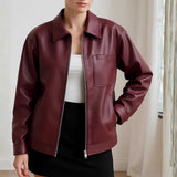 Person wearing a burgundy leather jacket indoors with a neutral background